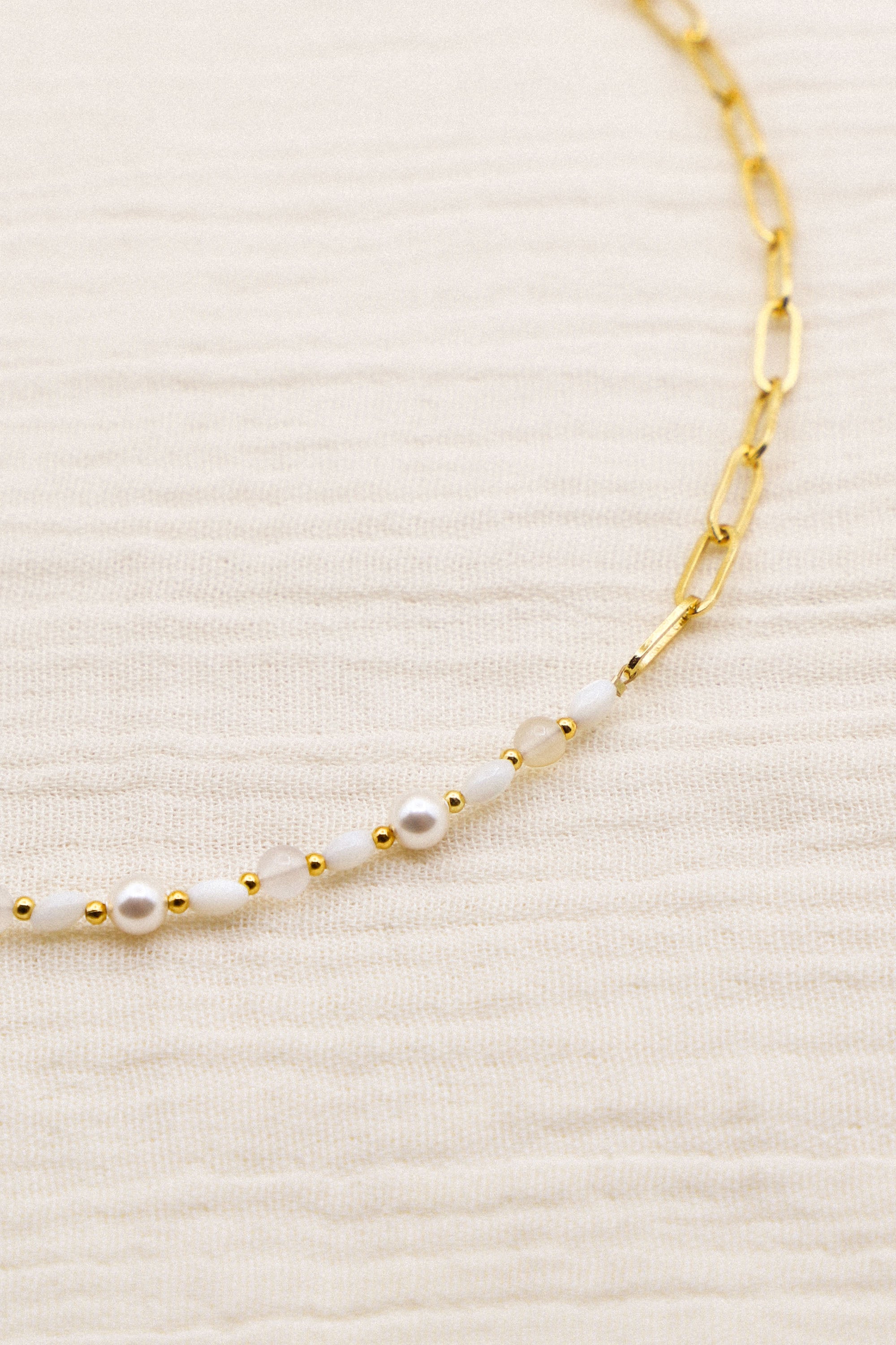 Collier Grace asymétrique, avec un côté perles et un côté chaîne. Les perles sont blanches et rythmées par de petites dorées.