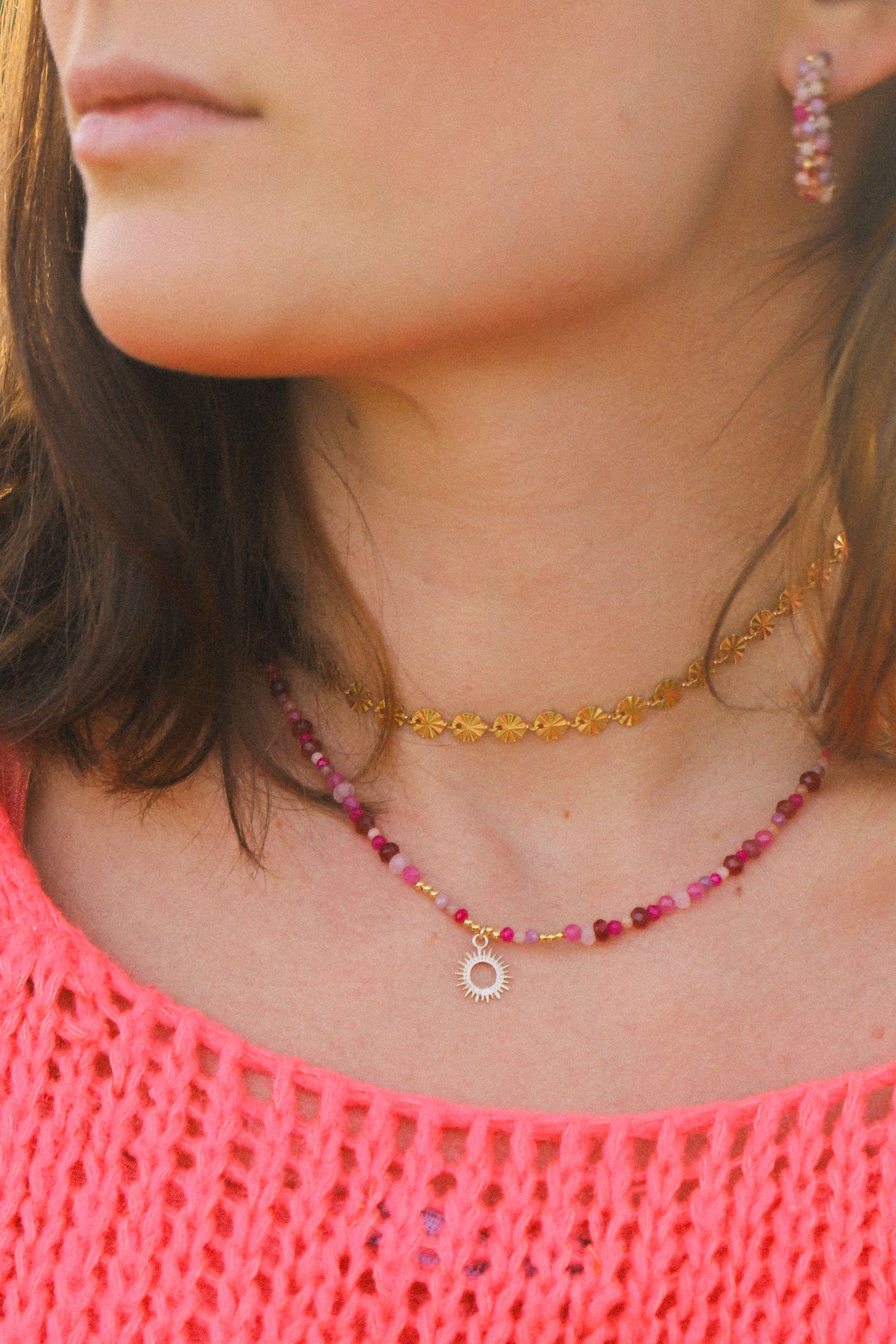 Collier Jane, ici porté, composé de perles roses et d'un petit soleil au centre.